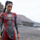Lauren Ridloff stands on a beach in her Eternals' costume as Makkari. The super-suit is red with grey accents and she has her hair in a high and long ponytail.